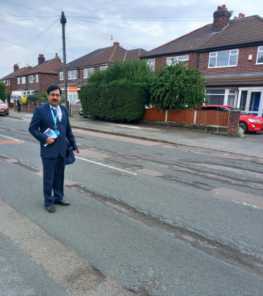 Councillor Kaushik Chakraborty standing over some potholes on Sinderland Road